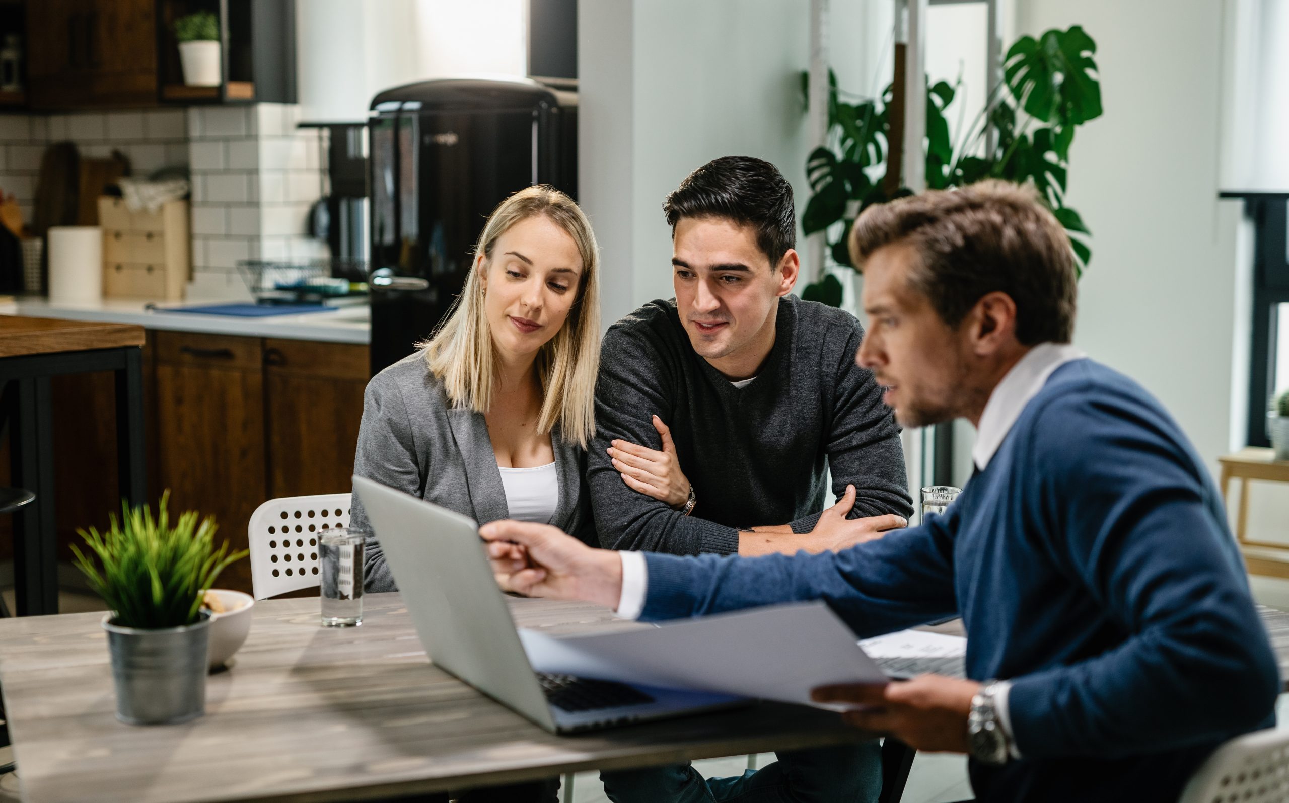 Young couple and real estate agent using laptop while going through housing plan on a meeting.
